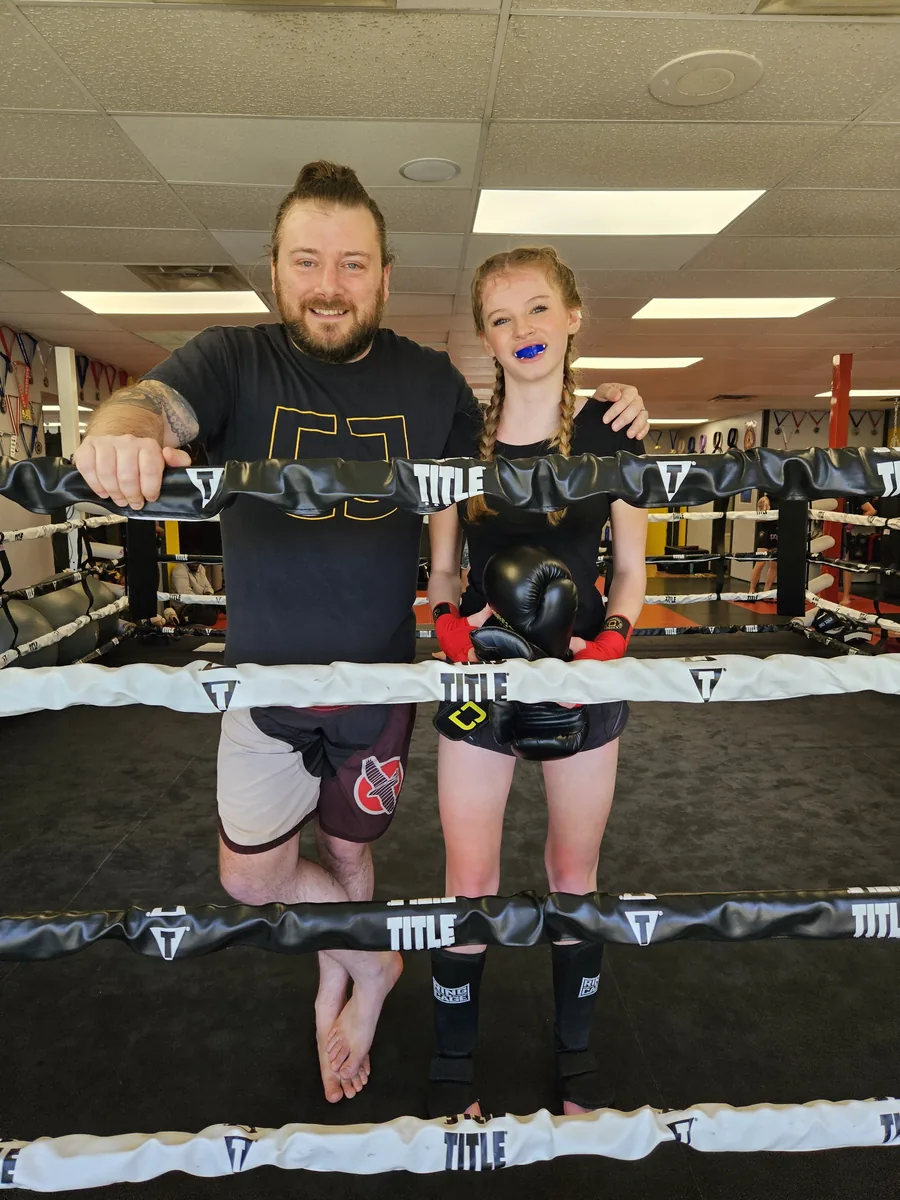 Jordy standing with a young student wearing boxing gloves in the ring.