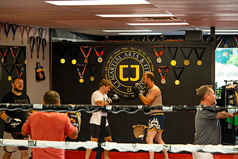 Two martial artists sparring in front of a CJ Martial Arts Nanaimo logo on a wall.
