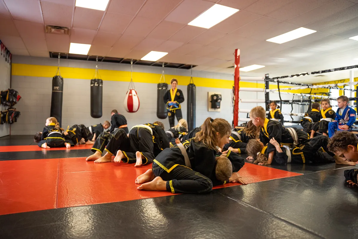 Young CJ Martial Arts students practicing Jiu-Jitsu on the mats while their instructor looks on